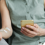 A woman comfortably receives IV therapy at home while using her phone.